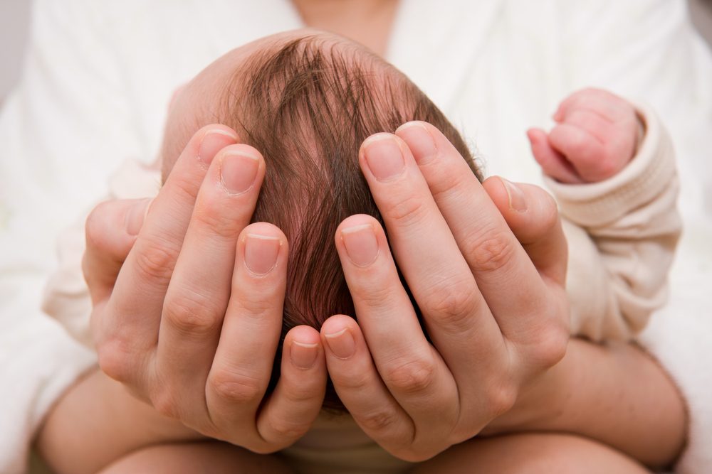 Practitioner cradling a newborn baby's head with both hands